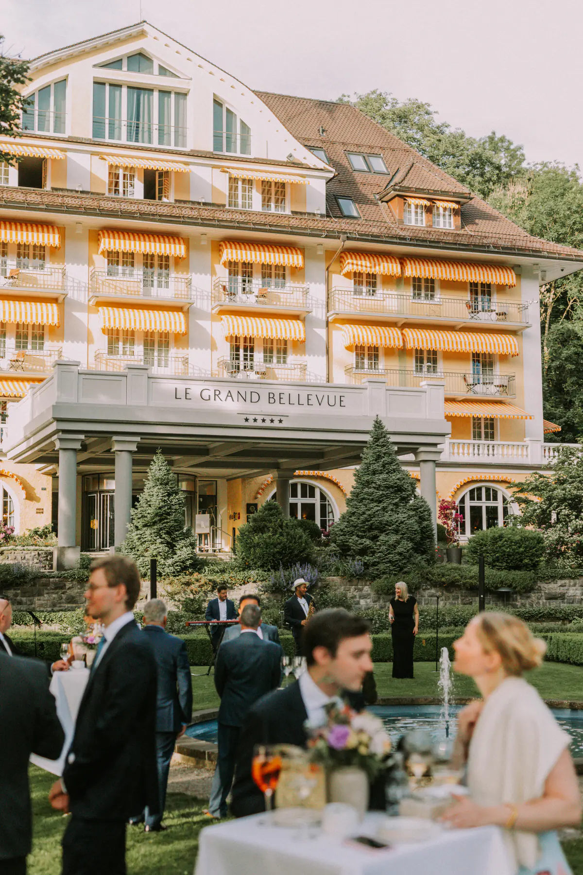 Invités en cocktail devant la façade et les balcons fleuris du Grand Hôtel Bellevue, à Gstaad