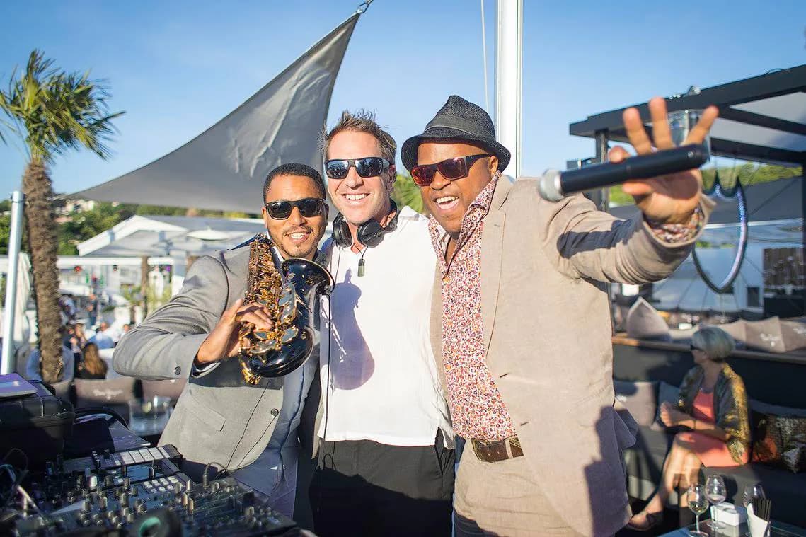 Trio d'artistes bras levés sur une terrasse ensoleillée